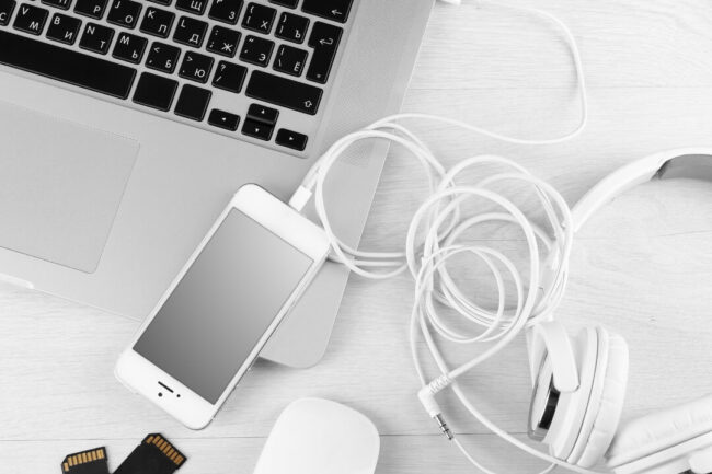 Blick auf den Schreibtisch, wo ein Laptop, ein Smartphone sowie Kopfhörer liegen