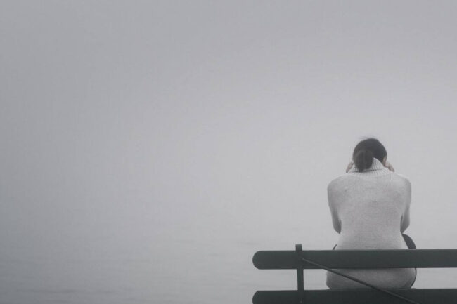 Einsame Frau sitzt auf einer Bank vor einer Nebelwand