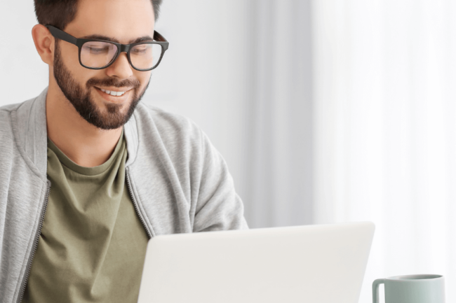 Lächelnder Mann vor dem Laptop in hellem Umfeld