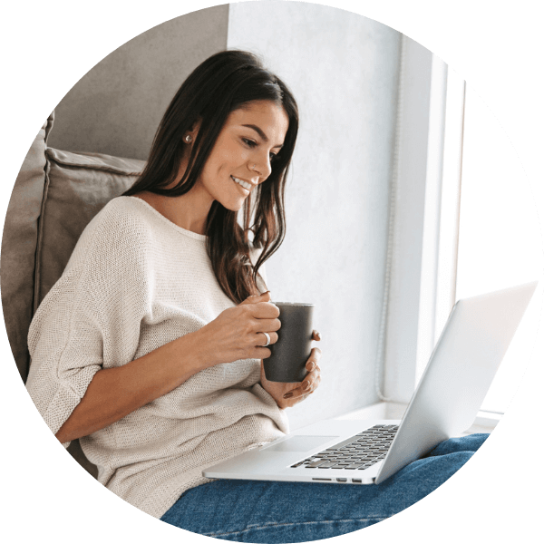 Glückliche Frau schaut auf ein Laptop und hat dabei eine Tasse Kaffee in der Hand
