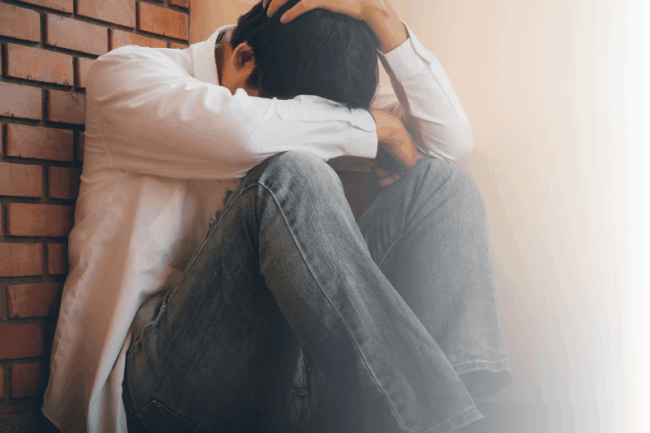 Trauriger junger Mann sitzt an der Wand