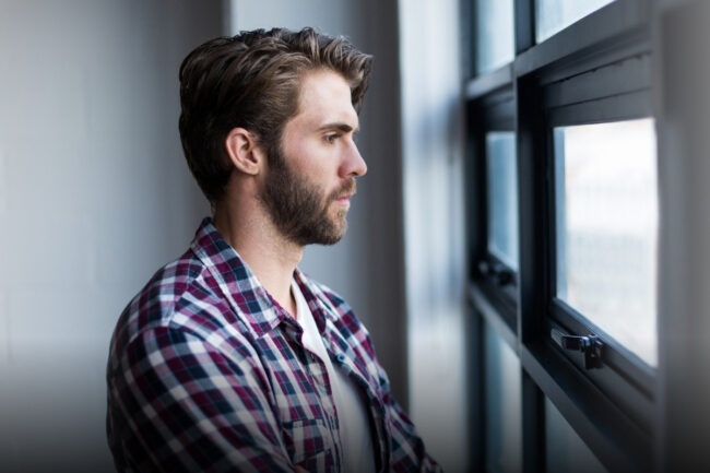Mann schaut nachdenklich aus dem Fenster