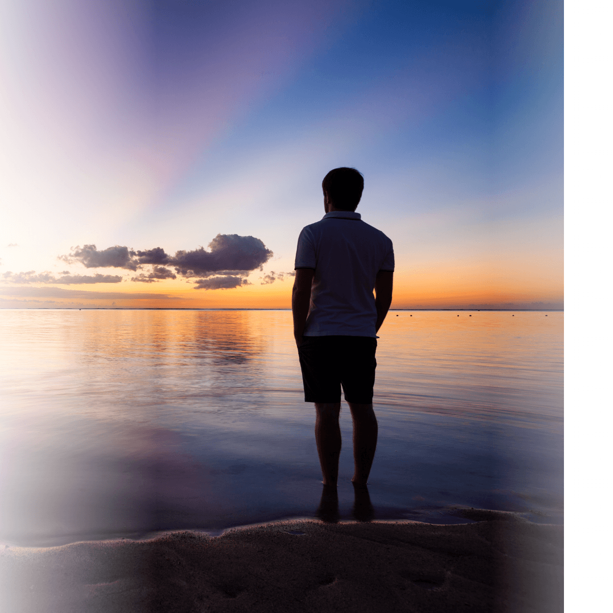 Mann steht am See und schaut auf den Horizont